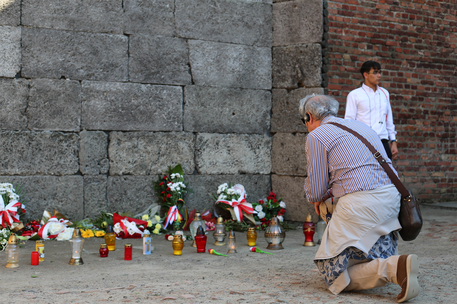 Visitor kneeling in tribute at the Death Wall with flowers and candles
