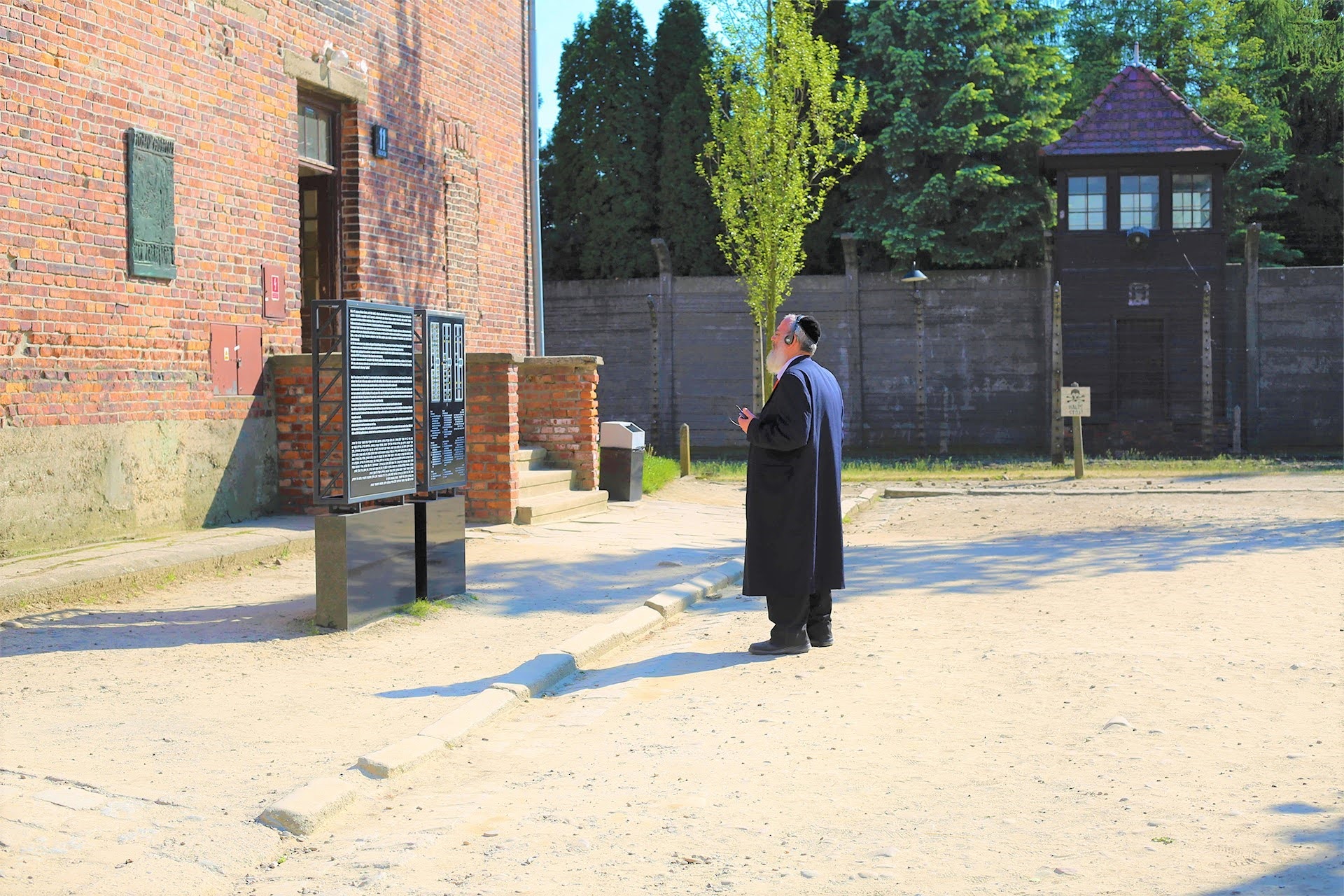 Visitor reading a memorial plaque near a watchtower at Auschwitz I